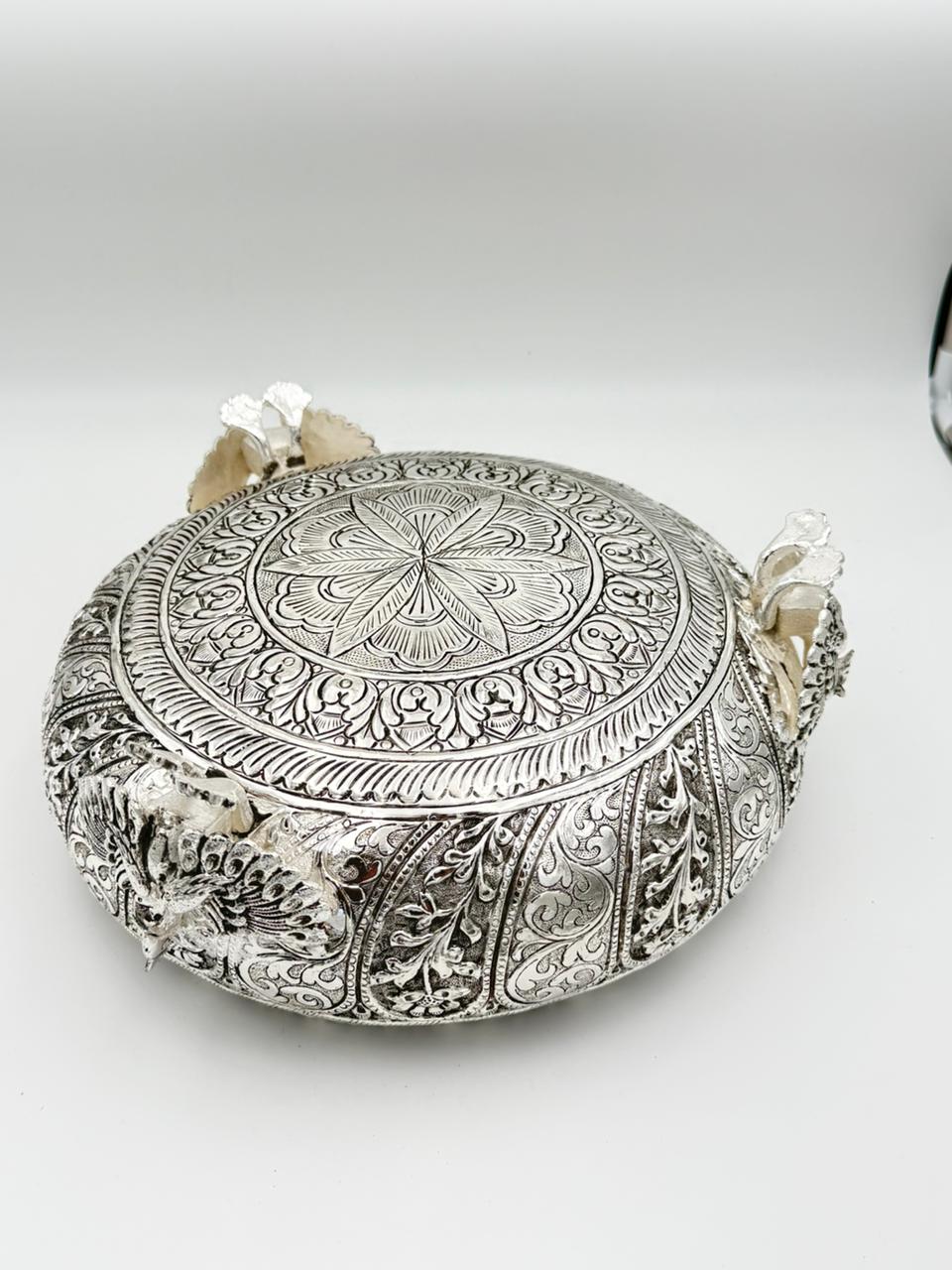 Handcrafted German silver urli bowl featuring intricate carvings and three peacock legs, ideal for floating flowers, candles, home décor, and traditional Indian festivals.