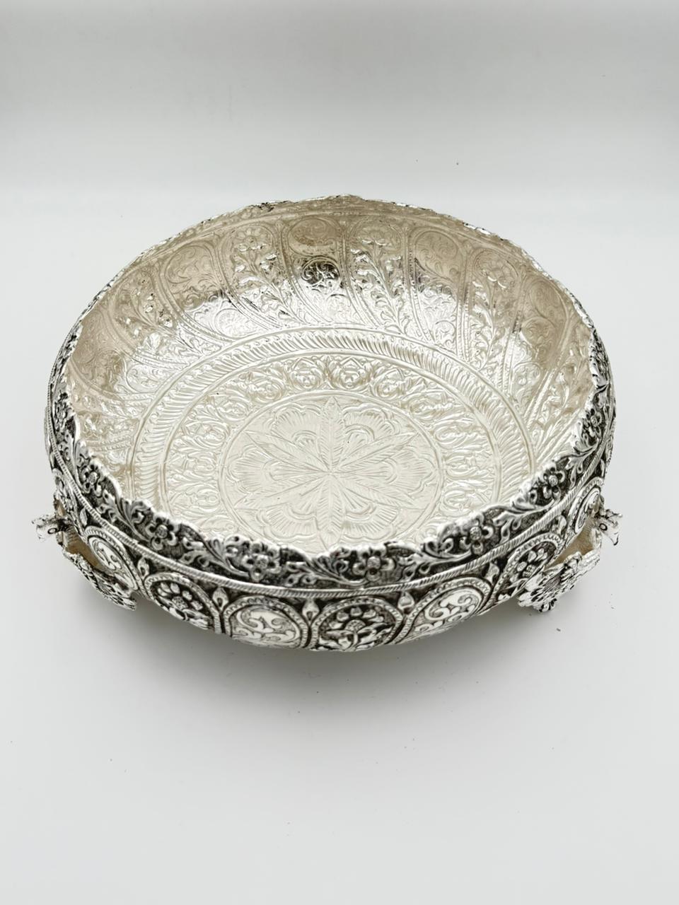 Handcrafted German silver urli bowl featuring intricate carvings and three peacock legs, ideal for floating flowers, candles, home décor, and traditional Indian festivals.
