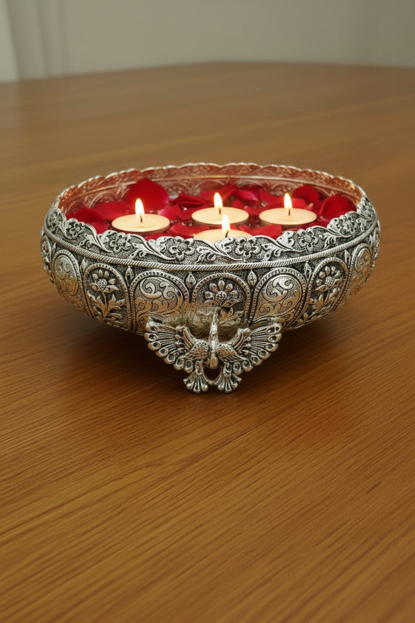 Handcrafted German silver urli bowl featuring intricate carvings and three peacock legs, ideal for floating flowers, candles, home décor, and traditional Indian festivals.